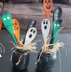 four halloween spoons with faces painted on them sitting in a cup filled with straw