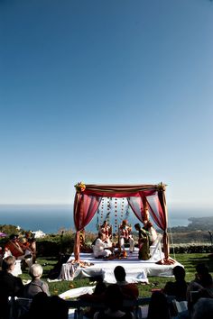 a group of people sitting on top of a lush green field under a blue sky