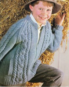 a young boy wearing a hat and sweater in front of hay bales with his hands on his hips