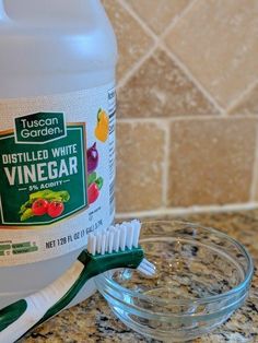 a bottle of distilled white vinegar next to a bowl with a toothbrush