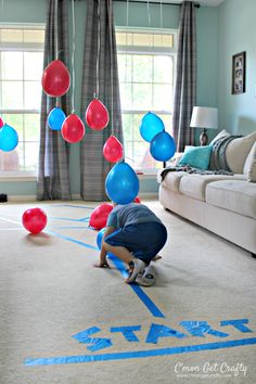 a boy is playing with balloons on the floor in front of a living room window