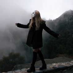 a woman wearing a mask standing on top of a mountain