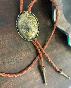 This awesome bolo tie has a southwestern design and genuine green/yellow jasper centerpiece. All stones will vary in grain/color. The cord is genuine brown leather with matching silver metal tips. Our bolos pair nicely with many of our belt buckles! They make wonderful gifts. The western bolo tie rope length is 40'' ; pendant size is 1 1/2'' x 1 1/4'' Bohemian Hand Tooled Jewelry For Rodeo, Rustic Adjustable Jewelry With Natural Stones, Adjustable Gold Jasper Jewelry, Western Style Gold Lariat Jewelry, Concho Jewelry For Rodeo, Southwestern Lariat Bolo Tie For Rodeo, Vintage Concho Lariat Necklace, Vintage Style Concho Lariat Necklace, Artisan Hand-tooled Jewelry For Rodeo