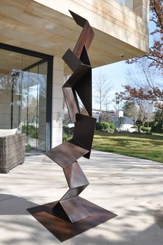 a metal sculpture sitting on top of a cement slab next to a building with glass doors