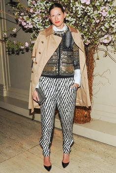 a woman standing in front of a vase with flowers on the wall and wearing pants