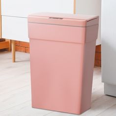 a pink trash can sitting on the floor next to a white cabinet and wooden floors