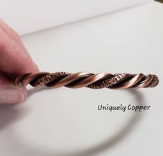 a person is holding onto a twisted ring on a white surface with the word unique copper written below it