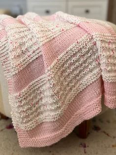 a pink and white knitted blanket sitting on top of a wooden chair next to a dresser