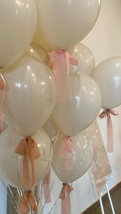 a bunch of white balloons with pink bows on them