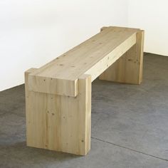 a wooden bench sitting on top of a cement floor next to a white wall in an empty room