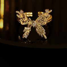 ✦ Indulge in the elegance of our Chunky 18K Gold Butterfly Cocktail Ring made with molten design and 18k gold plating. Perfect for any occasion, this statement ring features a bold butterfly design, adjustable fit, and serves as a luxurious gift for friends. Elevate your style with this exclusive piece that exudes sophistication and uniqueness. ----------- DETAILS ----------- - Color: Gold - Ring Size: 17.3mm (Approximately to Size US7) - Width: 1.8cm - Materials: 18K Gold Plated, Cubic Zirconia Gold Luxury Butterfly Ring For Formal Occasions, Luxury Gold Butterfly Ring As Gift, Luxury Gold Butterfly Ring For Formal Occasions, Gold Rings With Butterfly Charm As Gift, Gold Formal Butterfly Ring, Gold Rings With Butterfly Charm For Gift, Big Gold Butterfly Ring, Adjustable Gold Butterfly Open Ring, Adjustable Gold Butterfly Ring