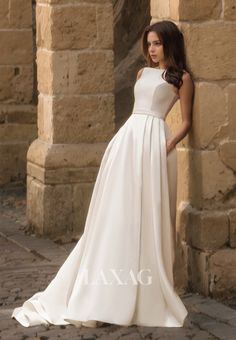 a woman standing in front of a stone wall wearing a white dress