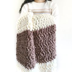 a woman is holding up a crocheted blanket