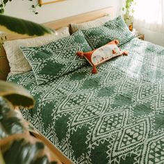 a bed with green and white bedspread next to a potted plant in front of a window