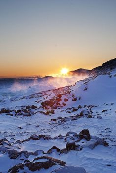 the sun is setting over some snow covered rocks