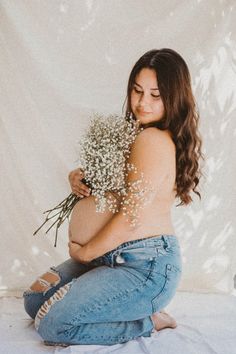 a pregnant woman sitting on the floor holding flowers