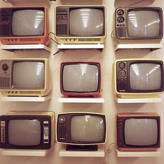 nine old televisions lined up in rows against a white wall with no one on them