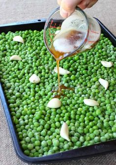 someone pouring sauce on peas in a pan