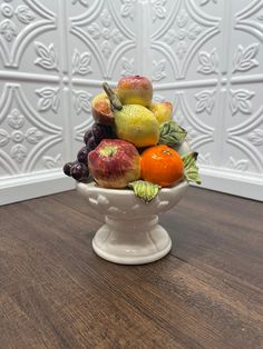 a white bowl filled with assorted fruit on top of a wooden table next to a wall