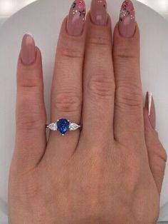 a woman's hand with pink and white nail polish holding a blue diamond ring