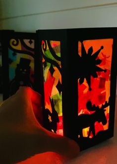 a hand holding a lit up box with animals on it's sides and an orange light in the background