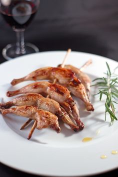 several pieces of meat on a white plate next to a glass of wine