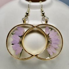 Real pressed lavender colored daisies are trimmed to fit the moon shaped bezel, then preserved in resin with green leaf accents to create this effortlessly whimsical statement. This dangly bohemian pair is lightweight, and can be worn all day without discomfort! They are made with hypoallergenic gold metal ear wire and crystal clear resin, allowing every detail of the daisy to be seen. This pair is customizable! If you would like a different color daisy or bezel, please let me know! While all pa Lavender Flower-shaped Earrings For Gifts, Lavender Flower Jewelry For Pierced Ears, Elegant Round Earrings With Pressed Flowers, Lavender Flower Jewelry With Matching Earrings, Lavender Flower Jewelry Set With Matching Earrings, Delicate Pressed Flower Earrings, Lavender Flower-shaped Jewelry With Birth Flower, Lavender Flower Jewelry With Pressed Flowers, Delicate Round Earrings With Pressed Flowers