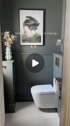 a white toilet sitting inside of a bathroom next to a painting on the wall above it