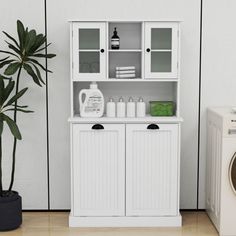 a white cabinet next to a washer and dryer in front of a green plant