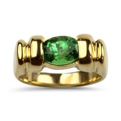 This stunning 14K yellow gold ring showcases an oval green tsavorite garnet, estimated at 1.7cts and measuring approximately 6x8mm, channel set east to west for a modern twist. The ring features a striking design with highly polished ridges on the face, measuring 7mm at its widest point and tapering to 3mm at the base of the shank. Size 6, this ring is stamped "MSJ 14K1," ensuring its authenticity. A perfect blend of elegance and contemporary style, this ring is an ideal choice for those who appreciate unique and vibrant gemstones.Replacement Value: $2,750.00 Classic Gold Ring With Tsavorite, Classic Yellow Gold Tsavorite Emerald Ring, Classic Yellow Gold Tsavorite Ring, Classic Oval Tsavorite Ring, Classic Oval Tsavorite Emerald Ring, Unique Garnet Ring, Tsavorite Garnet Ring, Tsavorite Garnet, Unique Jewelry Designs