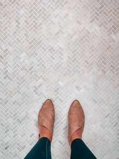 a woman's legs in green pants and heels standing on a white tile floor