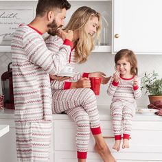 a man and woman in matching pajamas sitting on the kitchen counter with a child holding a cup