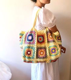 a woman is holding a crocheted bag in her left hand and wearing a white dress