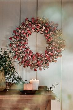 a wreath on a wall next to a table with two vases and a candle