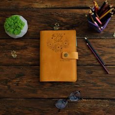 a brown leather notebook sitting on top of a wooden table next to some pencils