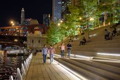 two people are standing on the steps by the water at night, with city lights in the background