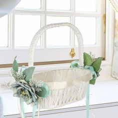 a white wicker basket with flowers and ribbons on the handle sits in front of a window