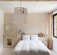 a white bed sitting under a large window next to a wooden ceiling light hanging from the ceiling