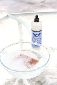 a bottle of alcohol sitting on top of a glass table next to a bowl filled with liquid