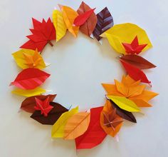 a wreath made out of folded paper with autumn leaves on the front and bottom, arranged in a circle