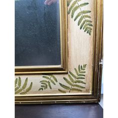 a painting with green leaves on it and a hand reaching for the reflection in the mirror