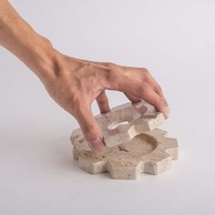 a hand reaching for a piece of stone that has been carved into the shape of a puzzle