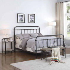 a bedroom with white walls and wood flooring has a metal bed frame, two nightstands, and pictures on the wall