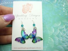 a pair of colorful butterfly shaped earrings on a card with purple and blue glitter nail polish