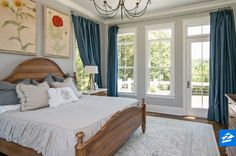 a bedroom with blue drapes and white bedding, chandelier, windows, and wooden furniture