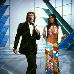 two people standing next to each other with microphones in their hands and one man wearing a tuxedo