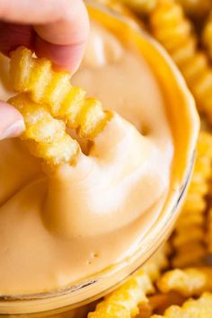 a person dipping cheese into a bowl of cheesy crackers with dip in the background