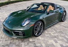 a green sports car is parked on a brick driveway in front of a house and trees