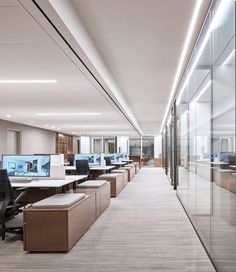 an office with rows of desks and computer screens on the wall in front of glass walls