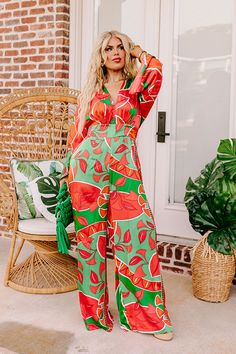 - This stunning jumpsuit is a ticket to sunshine vibes! Featuring a bold vibrant print and a chic satin finish, this trendy wide leg jumpsuit promises to steal the spotlight and keep you feeling fabulous. - Unlined material with a pink, orange, and green hued abstract botanical print with a satin finish - A v-cut neckline and a v-cut back with a tie detail - Long. loose sleeves - A waistline with an elastic back and an attached tie closure belt - A relaxed silhouette that ends in wide hemlines Chic Orange Jumpsuits And Rompers For Vacation, Chic Orange Jumpsuit And Romper For Vacation, Vibrant Jumpsuits And Rompers For Spring, Trendy Wide-leg Jumpsuits And Rompers For Vacation, Trendy Wide Leg Jumpsuits And Rompers For Vacation, Trendy Wide-leg Jumpsuits For Vacation, Chic Printed Jumpsuits And Rompers For Brunch, Chic Summer Jumpsuits And Rompers With Vibrant Print, Chic Wide Leg Jumpsuits And Rompers With Floral Print